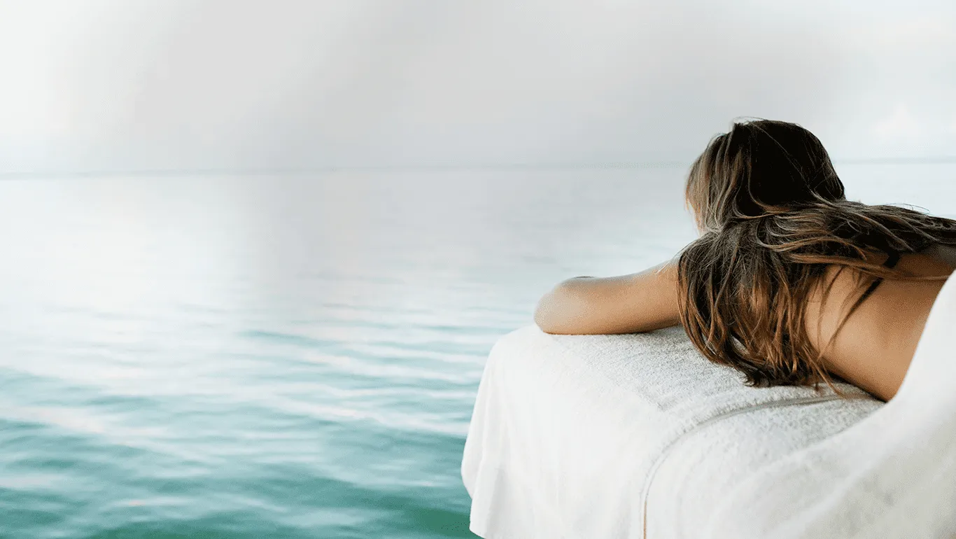 Woman resting on a massage table, gazing out over a calm sea